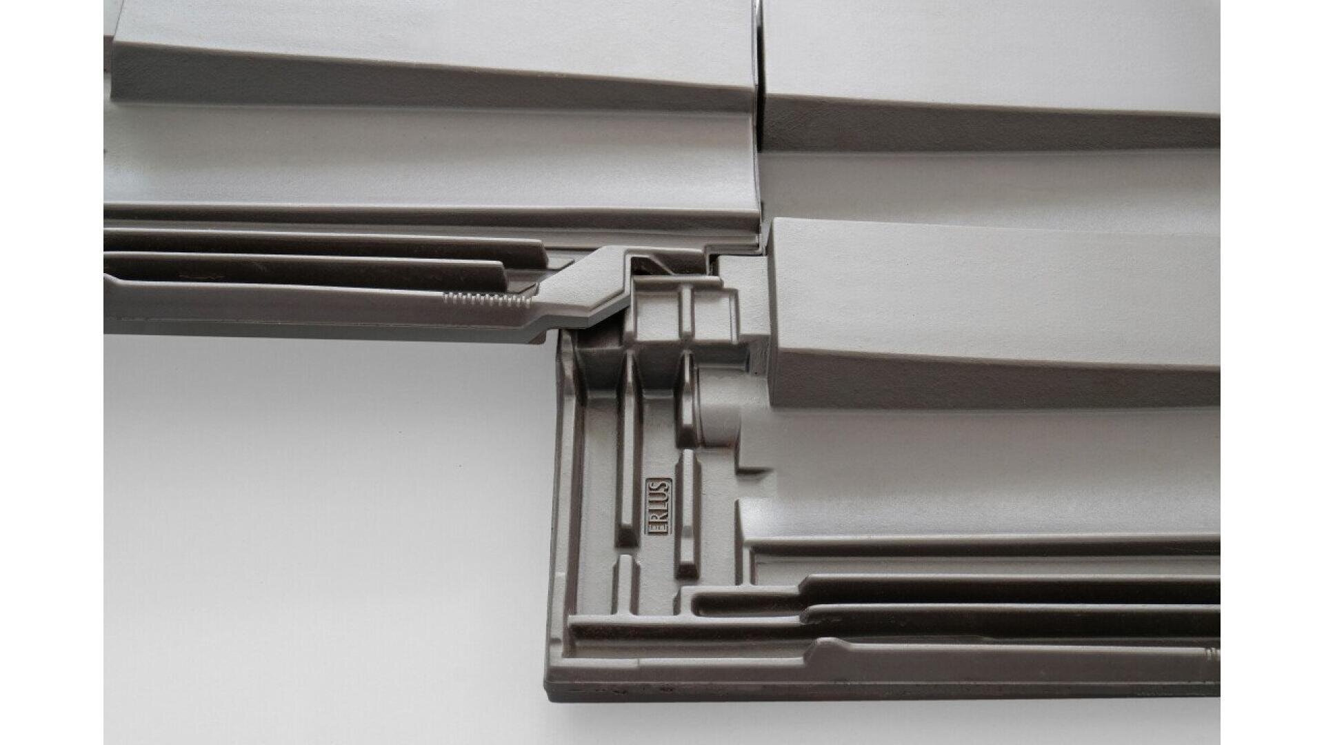Close-up view of interlocking gray roof tiles with clean, geometric lines. The tiles fit together precisely, showcasing their design for overlapping installation. The word RUBIS is stamped on one of the tiles.