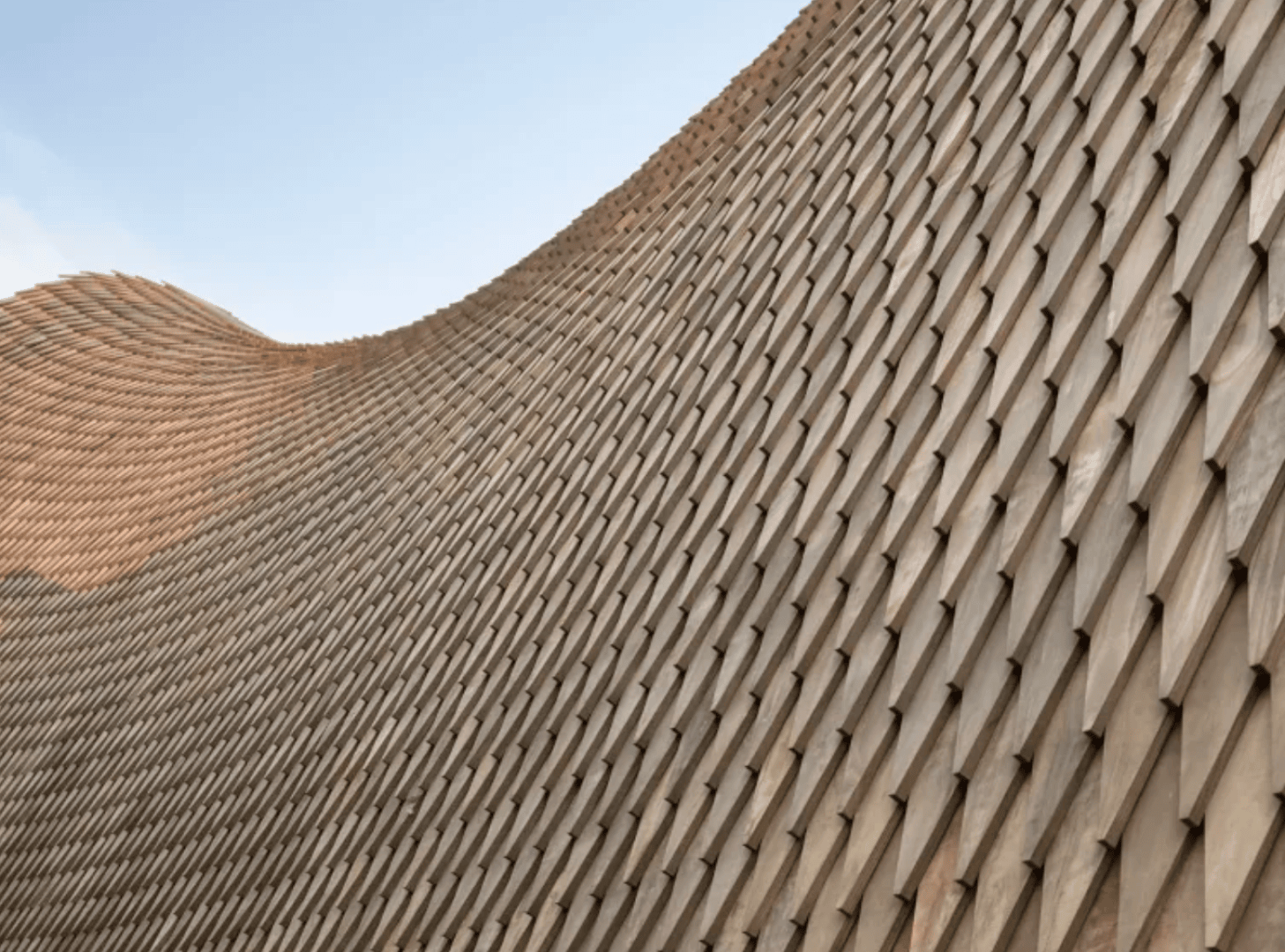 Close-up of a modern architectural structure with an undulating surface covered in repeating geometric tile-like patterns under a clear sky.