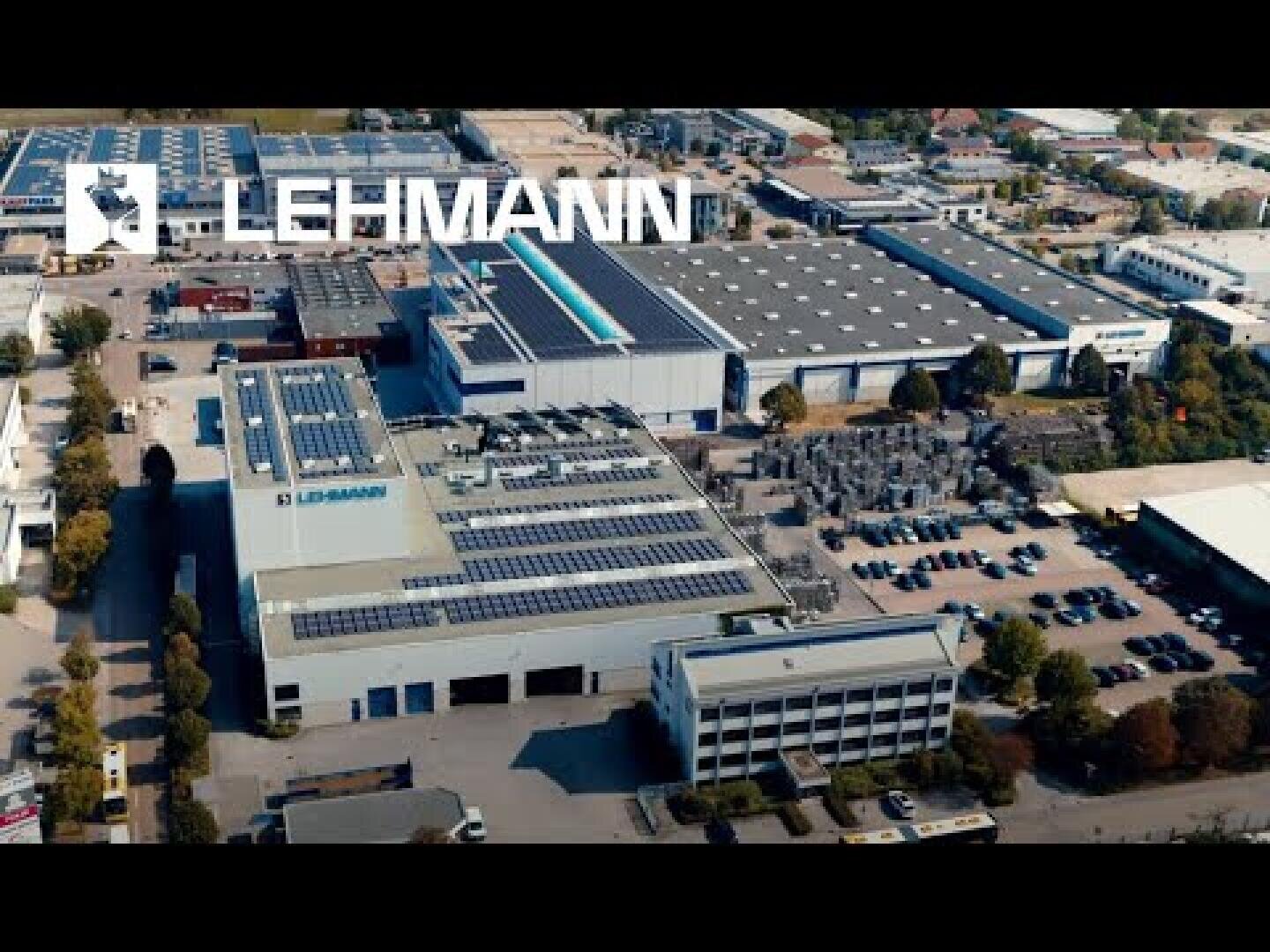 Luftaufnahme des LEHMANN-Industriegeländes mit mehreren großen Gebäuden mit Solarzellen auf den Dächern, Parkplätzen und umliegenden Grünflächen. Das LEHMANN-Logo ist im oberen Teil des Bildes gut sichtbar.