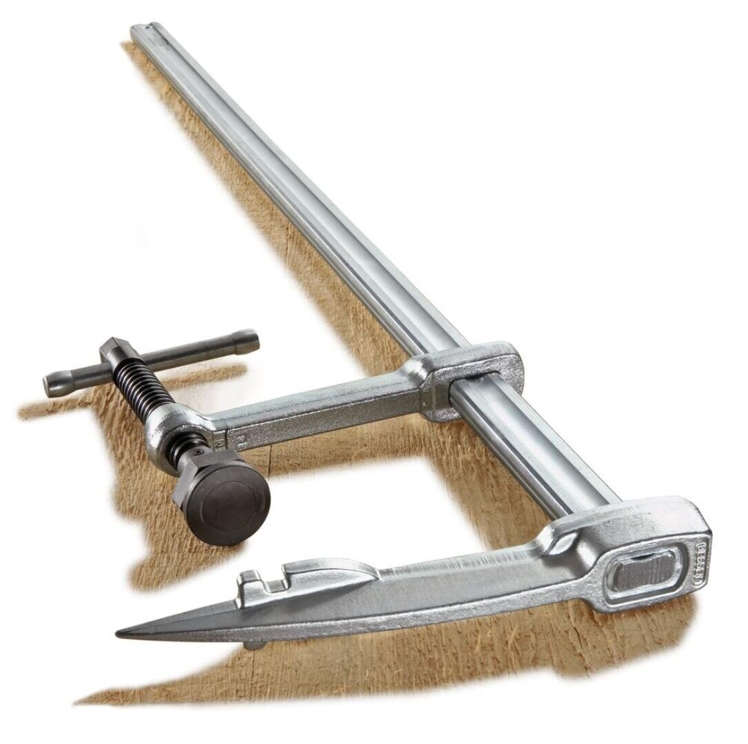 A metallic bar clamp with a screw handle securing a piece of wood, used for holding materials together during woodworking or construction tasks.