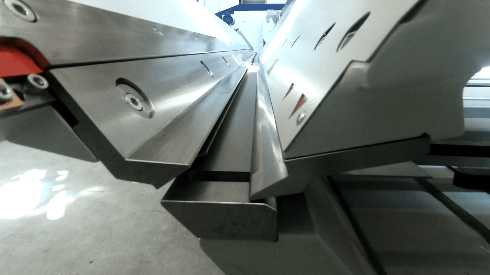 Nahaufnahme einer Blechbiegemaschine mit abgewinkelten Stahlplatten und Bolzen, die den Pressmechanismus in einer industriellen Werkstattumgebung zeigt.