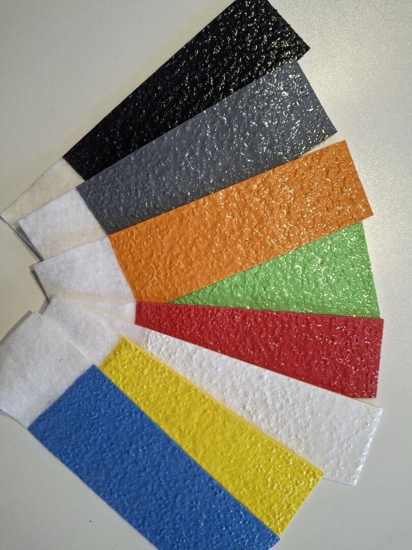 Acht strukturierte, rechteckige Streifen in Schwarz, Grau, Orange, Grün, Rot, Blau, Gelb und Weiß, aufgefächert auf einer weißen Fläche. Jeder Streifen hat eine glänzende, holprige Oberfläche.