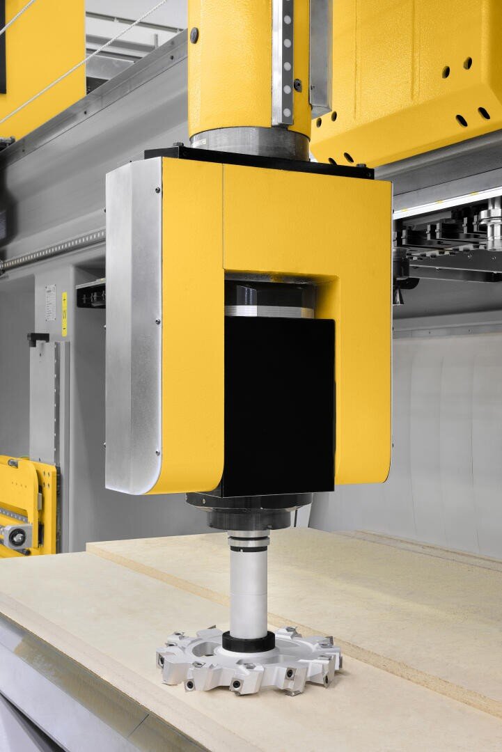 Eine Nahaufnahme einer gelben CNC-Maschine mit einem angebrachten Metallschneidwerkzeug, positioniert über einer flachen Holzplatte, bereit für die Präzisionsbearbeitung in einer industriellen Umgebung.