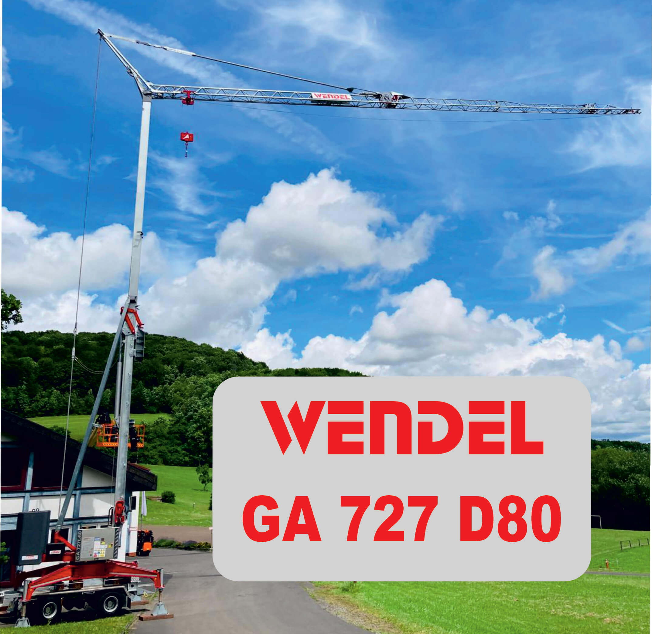 Ein hoher Baukran mit der Aufschrift WENDEL steht im Freien auf einer gepflasterten Fläche, mit grünen Bäumen und Gras im Hintergrund unter einem blauen Himmel. Der Text lautet: WENDEL GA 727 D80.