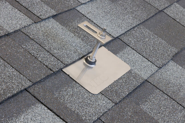 A metal roof bracket and a metal plate are installed on gray asphalt shingles, which are attached to the roof with screws to secure equipment or structures.